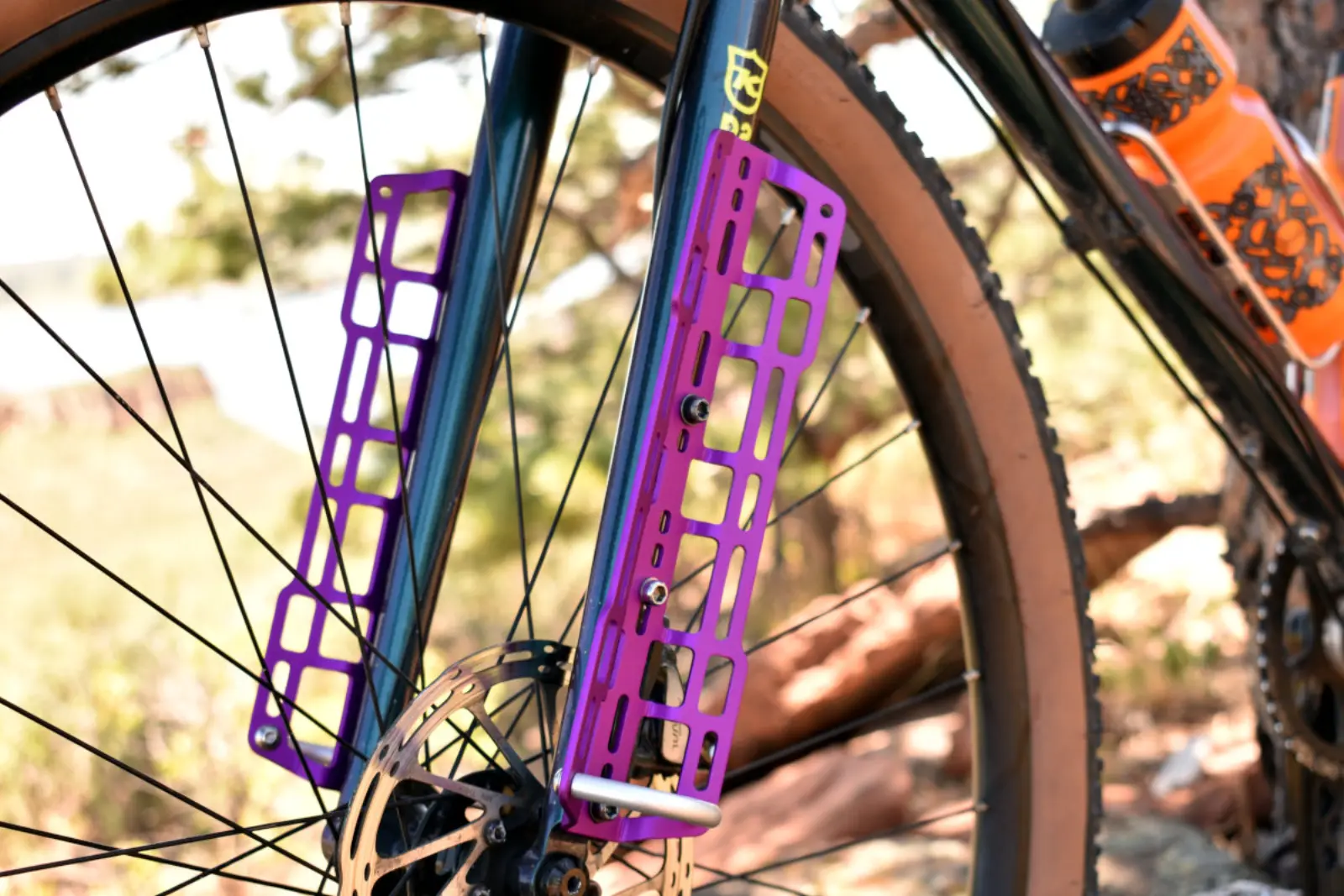 Purple anodised Widefoot CargoMounts bolted to a bike fork on a dirt trail