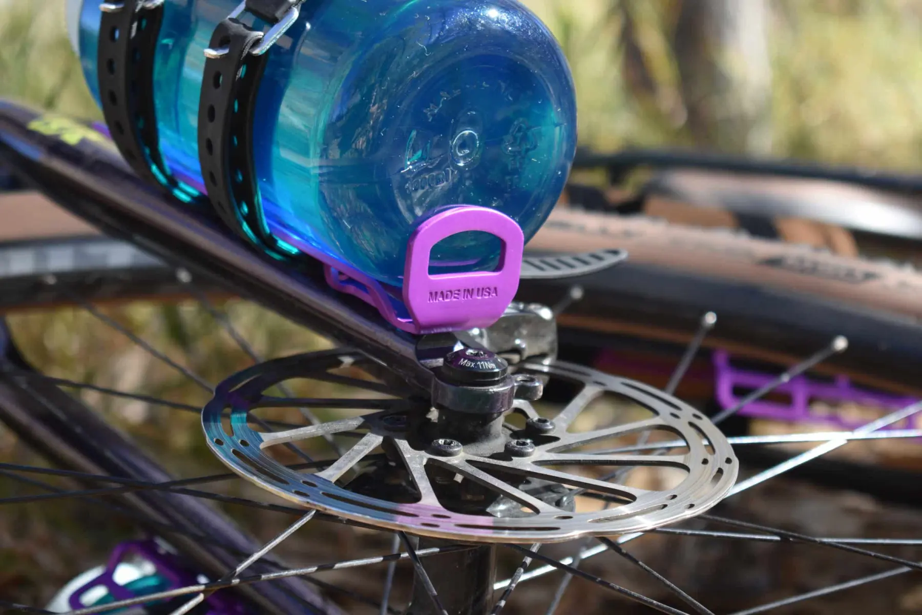 A Widefoot CargoMount in magenta anodised aluminium with MADE IN USA stamped into it, strapped to a bike fork holding a blue Nalgene bottle